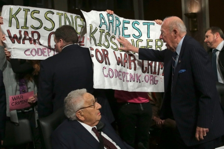 Der ehemalige US-Außenminister George Shultz (r) schiebt Demonstranten weg, die „Henry Kissinger für Kriegsverbrechen verhaften“ rufen, während der ehemalige US-Außenminister Henry Kissinger (l) zuschaut, bevor die beiden vor dem Senatsausschuss für Streitkräfte am 29. Januar 2015 in Washington, DC aussagen.